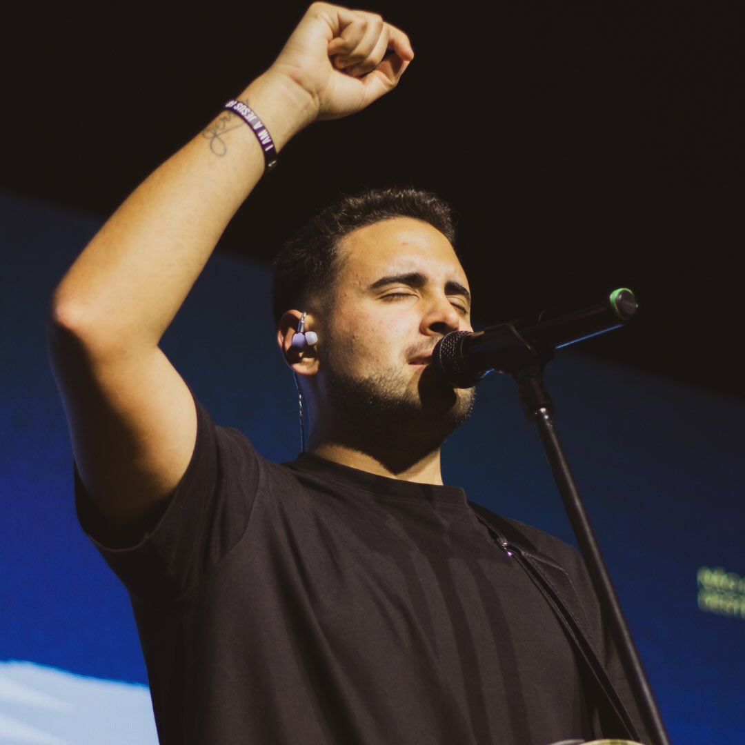 Lucas Oliveira em adoração, mão erguida ao microfone